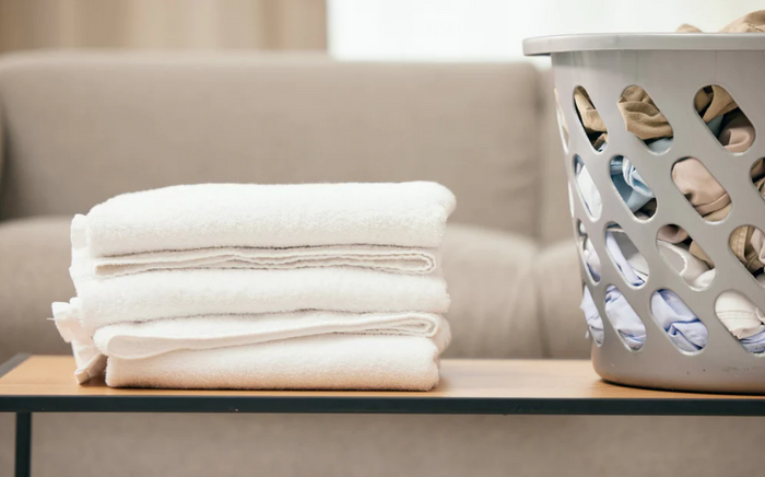 Folded towels on a coffee table next to a basket of laundry.