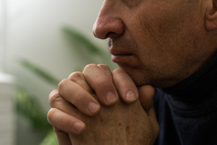 A man rests his head on clasped hands.