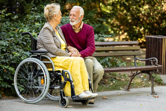 A couple in a park, one in a wheelchair and one sitting on a bench.