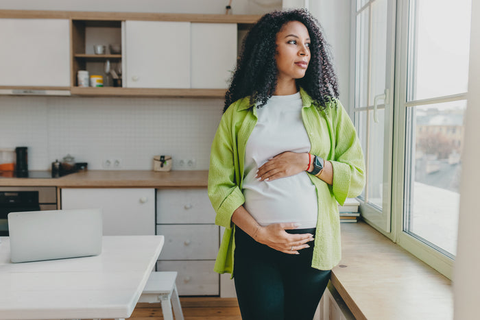 A pregnant woman looks out a window.