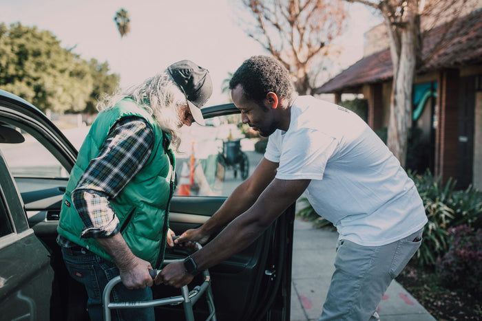 A man helps another man with his walker.