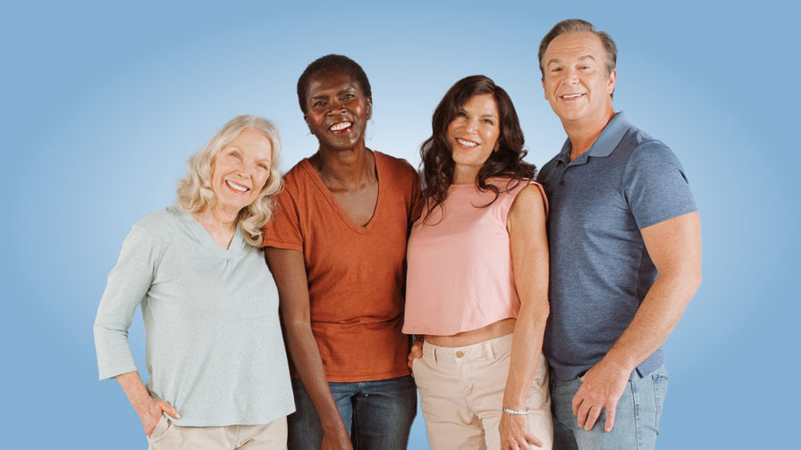 Four older adults stand smiling together on a solid blue background.