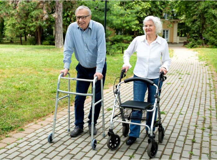 A man and woman walking with rollators on a brick path.