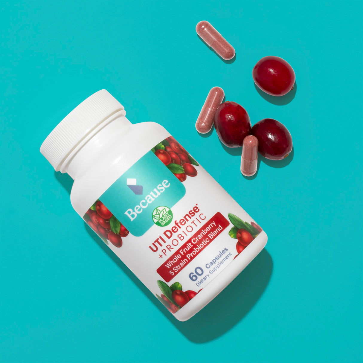 A white supplement bottle with cranberries on the label and red supplements spilling on to a blue surface next to cranberries.