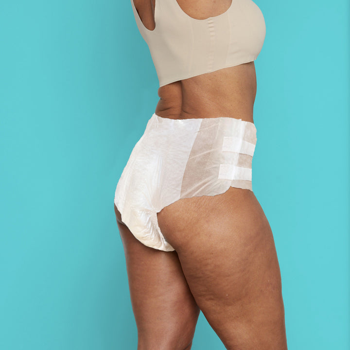 Back view of woman wearing Because Maximum tabbed briefs on teal background