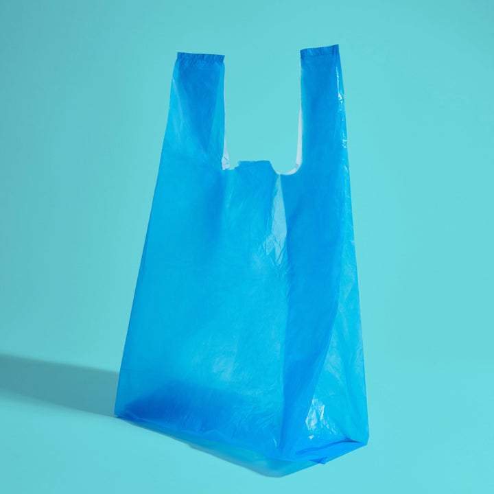 A blue opaque Because disposal bag with long tie handles on teal background