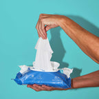 Hands pulling out Because cleansing wipes from package on teal background