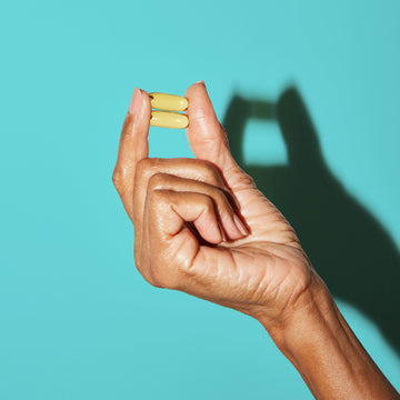 Hand pinching 2 omega 3 gel capsules between her fingers.