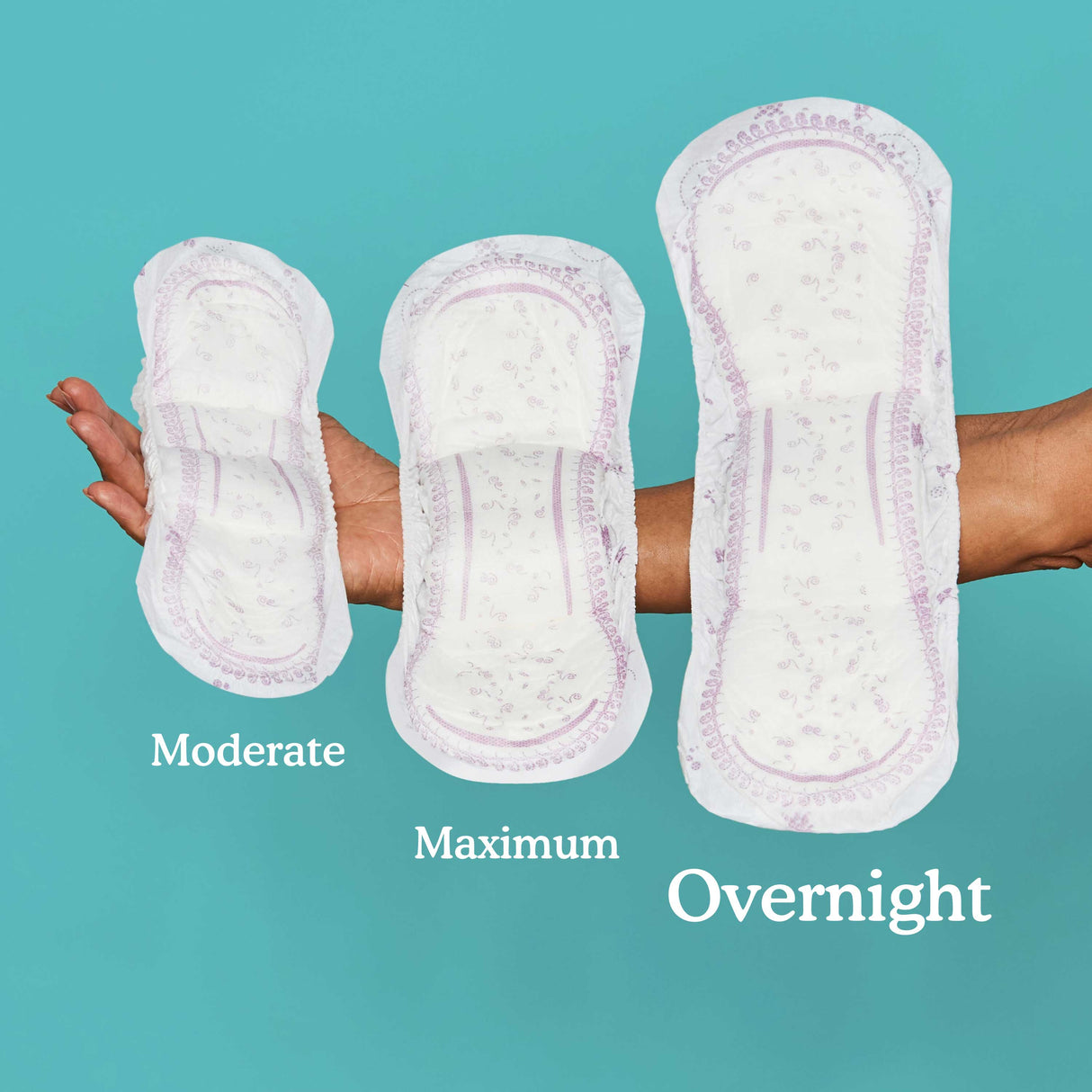 A woman holding a moderate, maximum, and overnight pad in her arm with the overnight pad being the largest