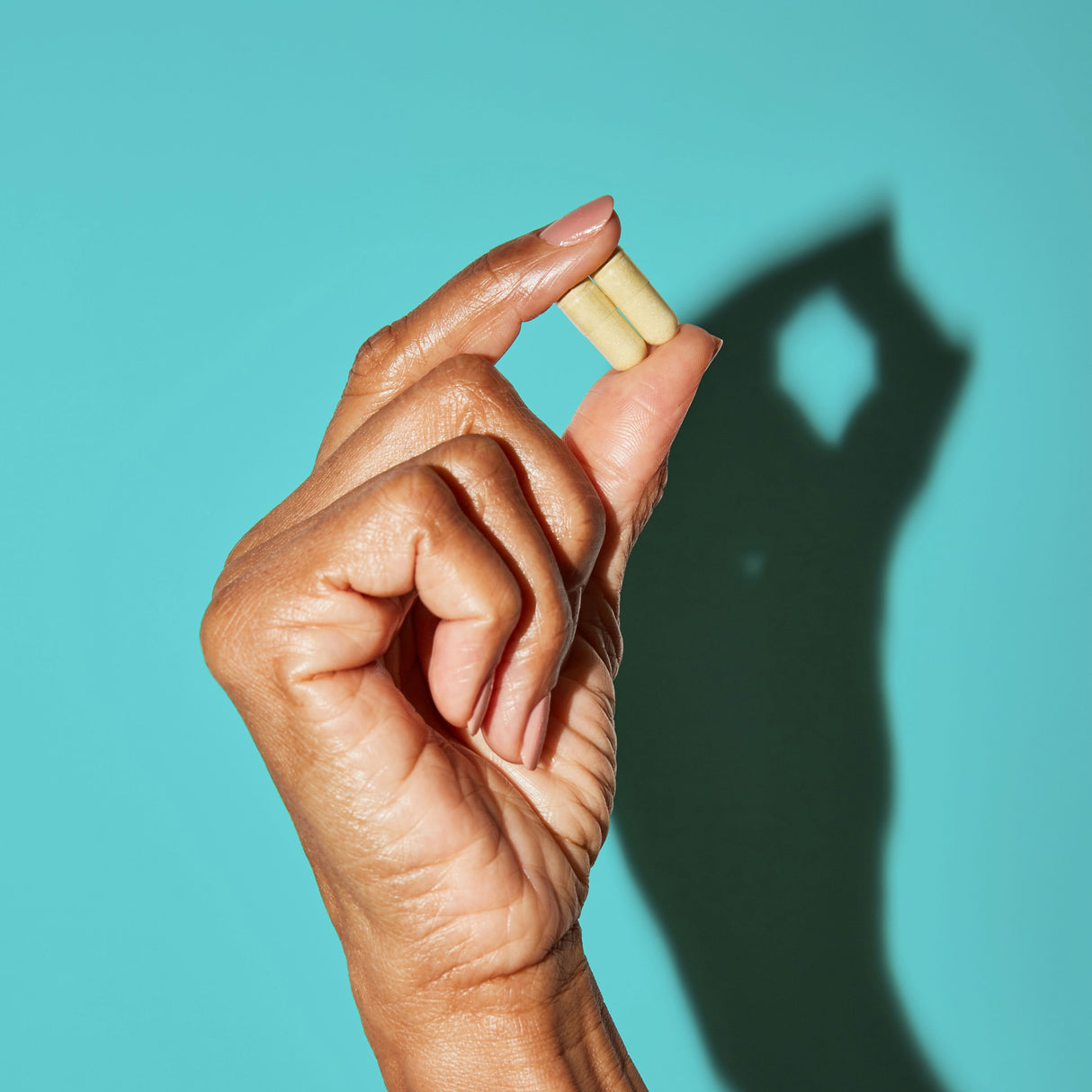 Woman holding two yellow capsules between her fingers
